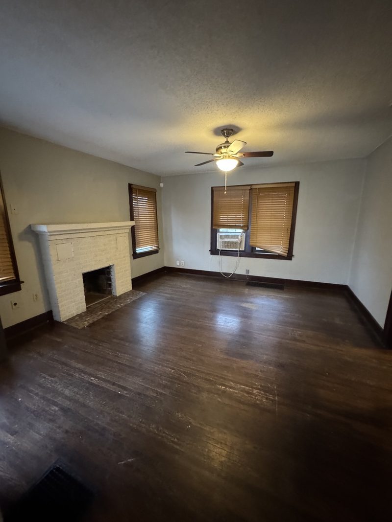 Before: empty living room with a dated fireplace, dark floors, and window AC unit