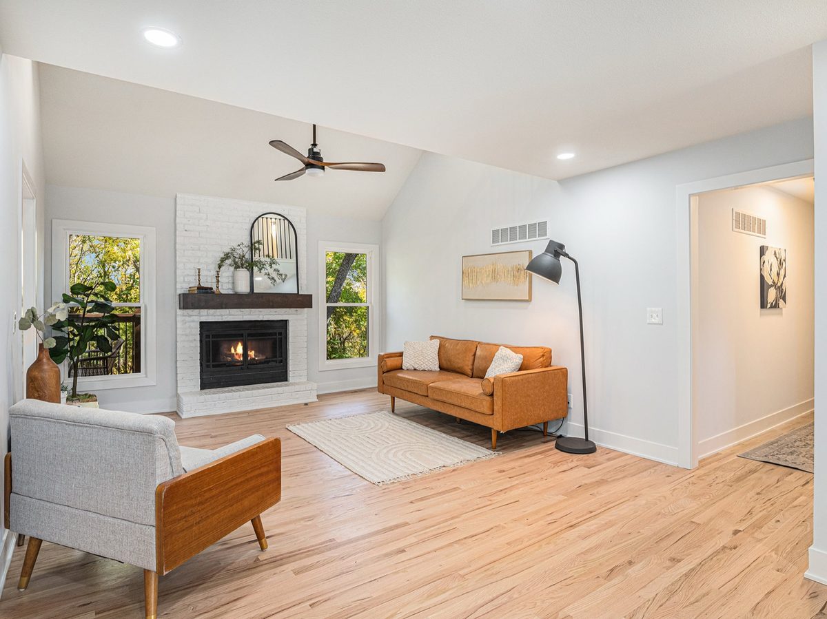 After: bright vaulted great room with a white-painted brick fireplace and light wood floors