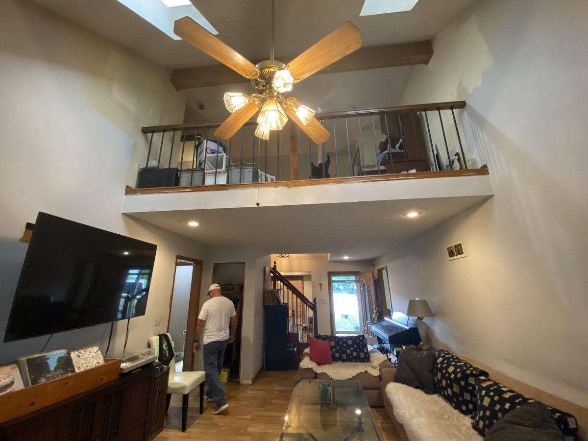 Before: dated vaulted great room with dark trim, a loft railing, and worn walls