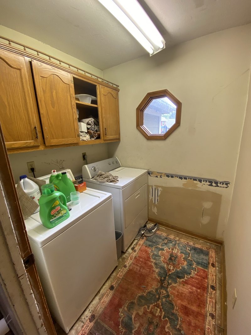 Before: dated laundry room with oak cabinets, a duck wallpaper border, and an octagon window