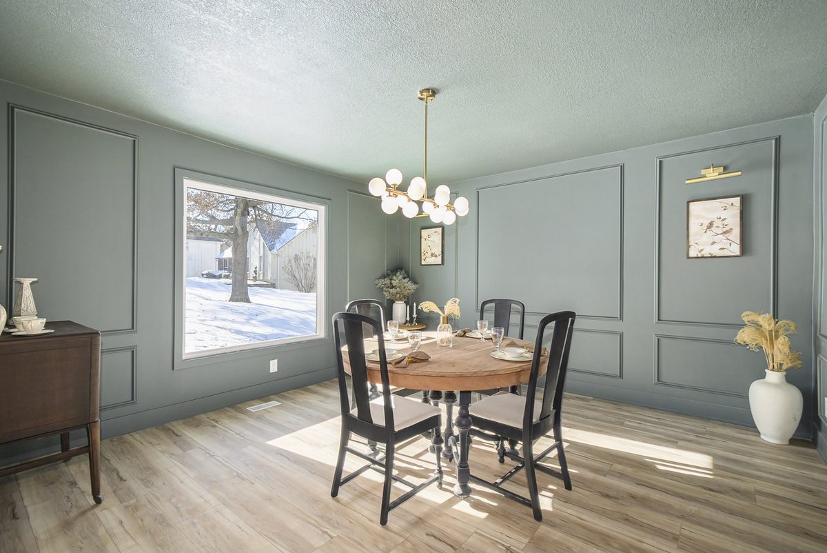 After: dining room in deep sage with picture-frame molding, wood floors, and a staged round table