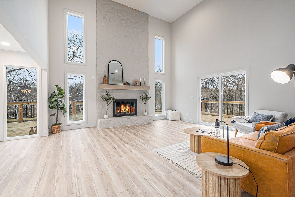 After: bright vaulted great room with a light plaster fireplace, wood mantel, and warm wood floors