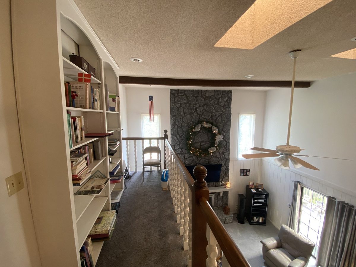 Before: two-story great room with a dark floor-to-ceiling stone fireplace and a beamed, popcorn ceiling